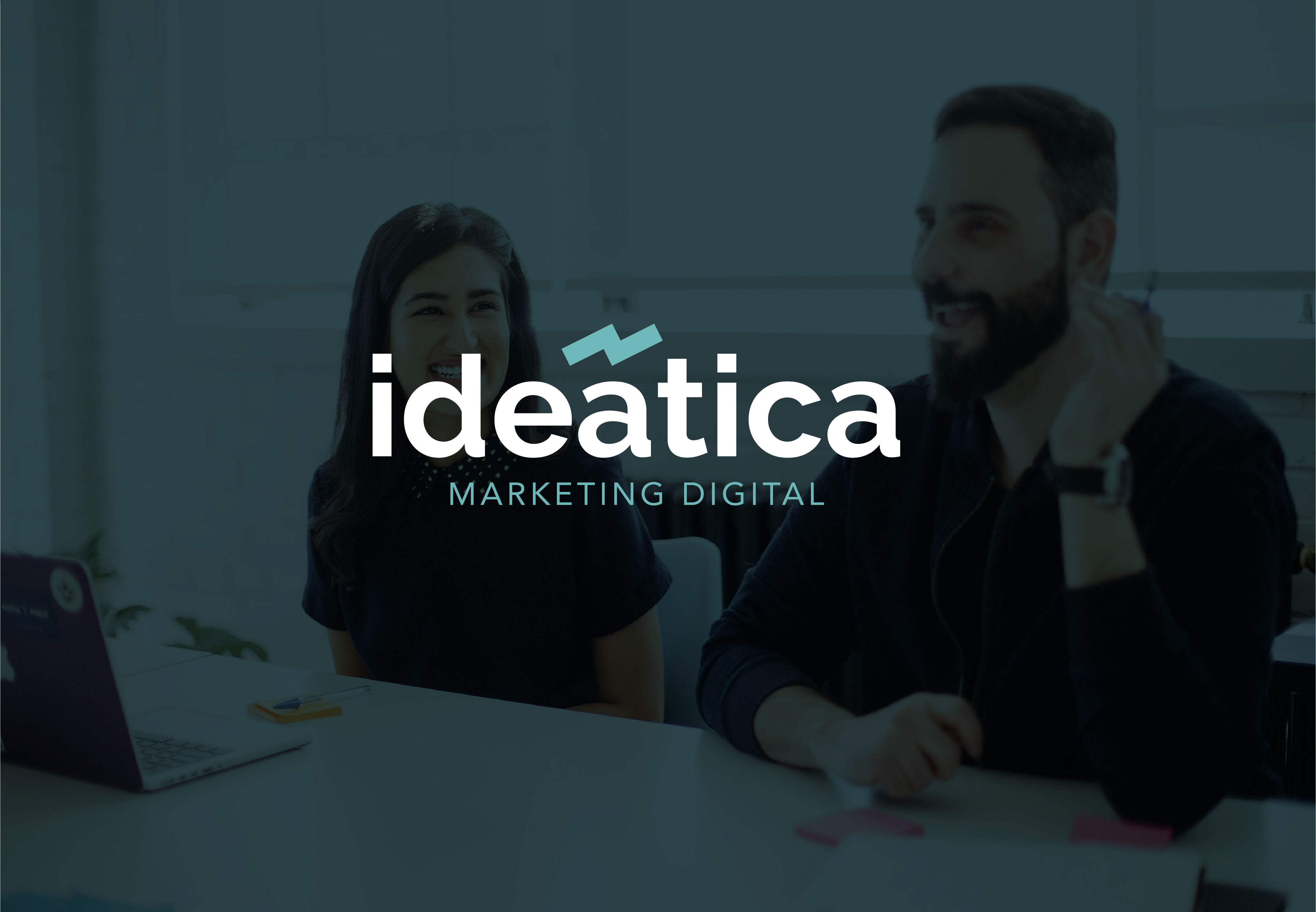 Imagen que muestra logotipo de agencia de marketing, "ideática". Como fondo de la imagen una fotografía de una situación de trabajo en equipo de la agencia.